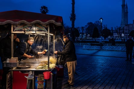 A man who has undergone a hair transplant buys corn on the cob in the evening in Sultan Ahmet Park
