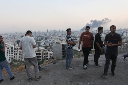 A group of men look at smoke rising above a city