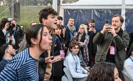Two young people stand and shout towards the stage as others film them on their phones and take photos.