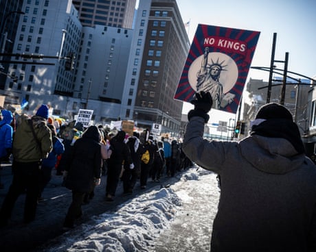 A person holds a ‘No Kings’ sign outside as people march