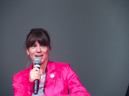 A person wearing a bright prink jacket, holding a microphone