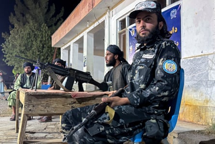 Two bearded Afghan men sit with assault rifles on their laps