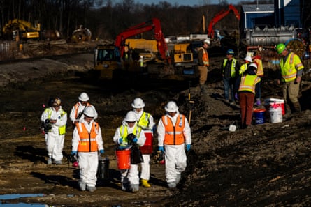Workers in hazmat suits walk in a field