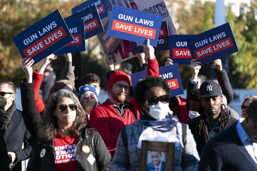 A crowd of people attend a rally, all holding signs which read 'Gun laws save lives'.