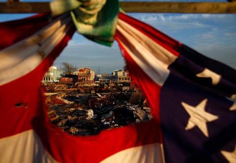 Homes destroyed during Hurricane Sandy are framed by a tattered American flag.