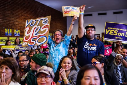 A group of people in a building cheer and hold up banners during a campaign event in support of Proposition 50