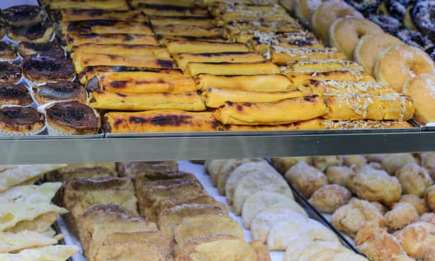 A close up view of Portuguese tarts, doughnuts and pastries on display in a bakery shop window.