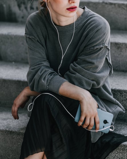 Young woman with mobile phone sitting on the stair in the city and listening music on earphones.