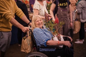 A woman in a wheelchair carries a number of potted plants and smiles broadly.