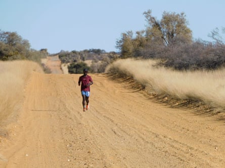 A man runs on a dusty empty road through dry savanna