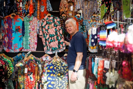 Adrian Chiles looks sceptical as he holds a Hawaii-style shirt in a shop at Glastonbury
