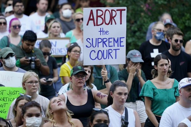 A large group of people stand together holding signs, the biggest proclaiming ‘Abort the supreme court’.