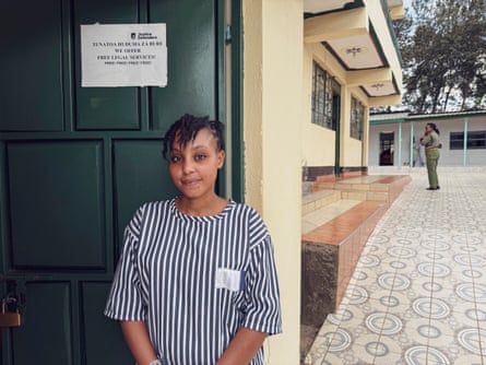A woman in a striped dress stands in front of a green door, while a prison officer can be seen in the background.