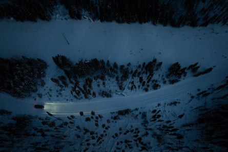A truck drives down a winter road connecting Pickle Lake and Cat Lake First Nation in Ontario. Its headlights shine in the dark as it travels in the snow between trees.