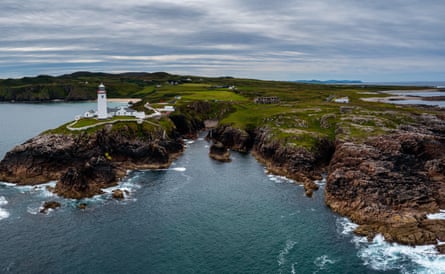 White lighthouse on green and rocky peninsula/headland