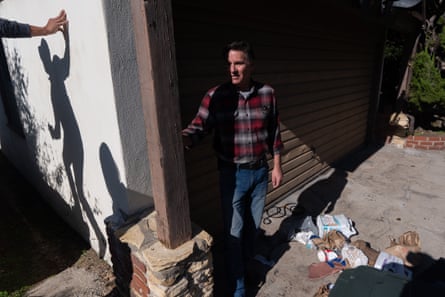 Man in flannel shirt stands in sharp sun with food garbage on cement driveway beside him.