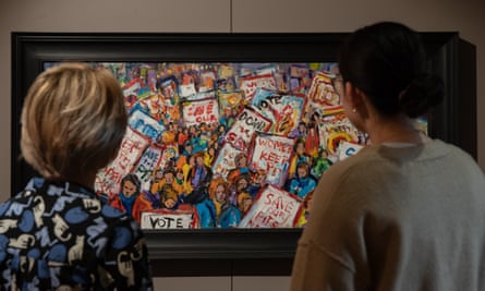 Two people look at a framed painting of a protest in which people are holding signs such as ‘Save our pits’