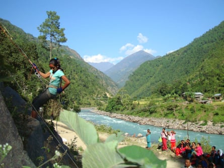 A small group of people look on as a woman abseils down a steep slope