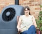 Clare Naylor smiles in a garden chair beside her home's heat pump unit