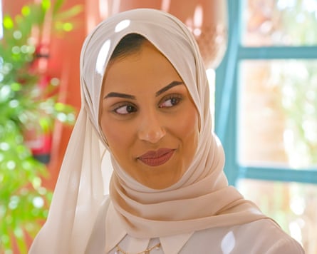 A woman in a hijab smiles while looking to the side.