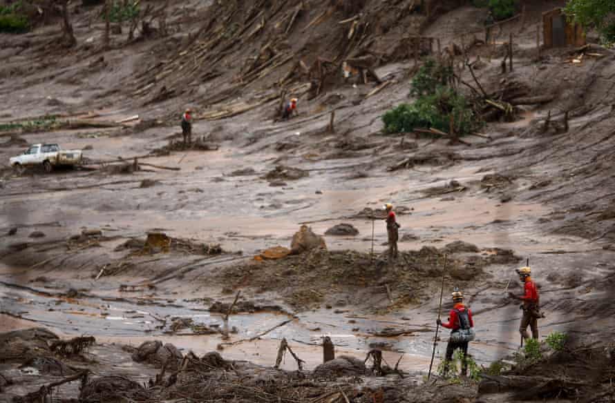 Equipes de resgate em um mar de lama com uma caminhonete meio enterrada ao fundo.