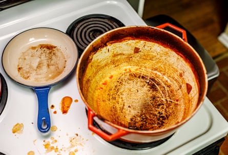 The remains of something that was fried is stuck to the bottom of a non-stick frying pan. Sloppy splotches of tomato sauce are splattered all over the electric stove top surface
