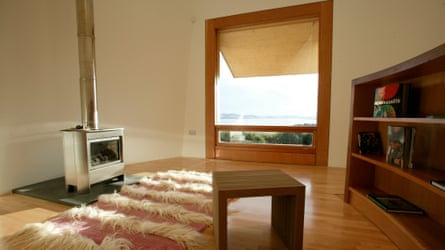 The upstairs tower room, with a large window, wood burner, shelves and a small table, decorated in warm tones