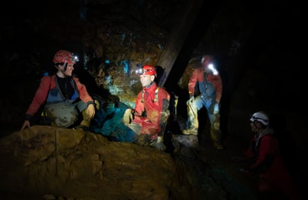 Four people with helmets and head torches sit in the dark on rocks.