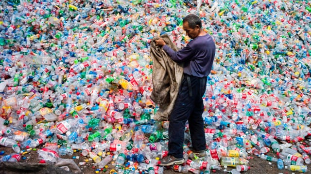 man standing in front of a mountain of plastic waste Kurangi penggunaan plastik