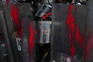 A police officer in riot gear looks out from between shields smeared with red paint