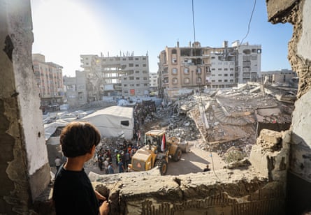 A young child watches from a nearby building as rescue workers search the rubble.