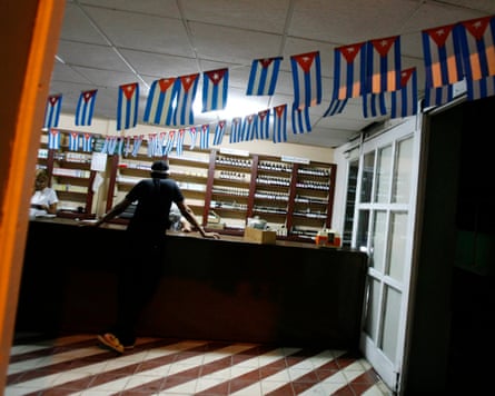 a man stands at the counter of a pharmacy adorned with Cuban flags