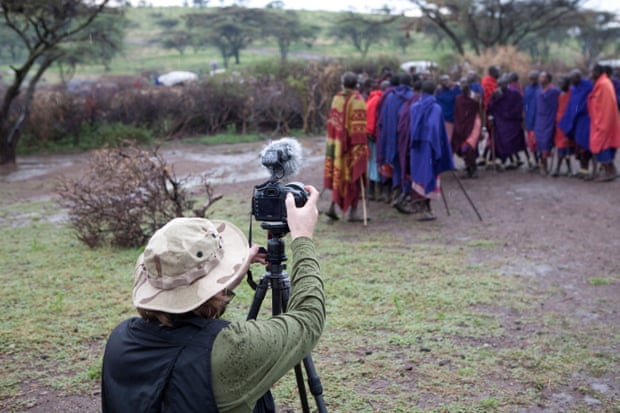 A tourist takes pictures of Maasai villagers.