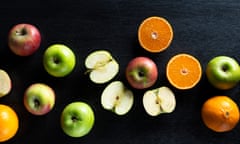 Overhead shot of whole and halved oranges and apples on a black surface