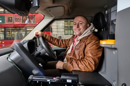 Ben McMullan at the wheel of his taxi. He wears a brown leather jacket and is smiling.