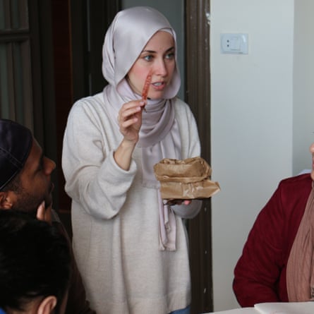 A woman in a hijab holds up an ear of grain while she talks to people sitting round a table 