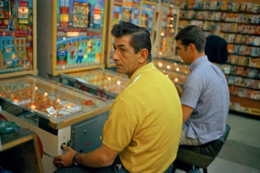 A dark-haired man in a yellow shirt and a dark-haired man in a blue shirt sitting at a pinball machine