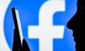 silhouette of woman holding mobile phone in front of a large facebook sign