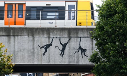 A mural of three monkeys swinging across a bridge with a train passing overhead
