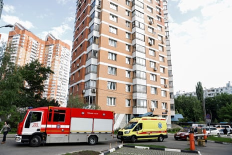 An ambulance and firefighting vehicles are parked outside a multi-storey apartment block following a reported drone attack in Moscow.