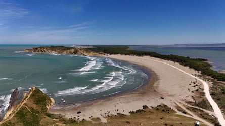 An aerial view showing the sandy beach in a bay along a narrow strip of land in a blue sea.