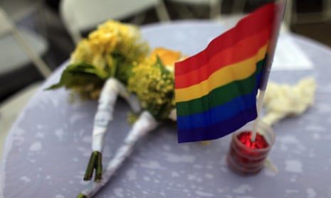 A gay pride flag stands on a table next to two wedding bouquets.