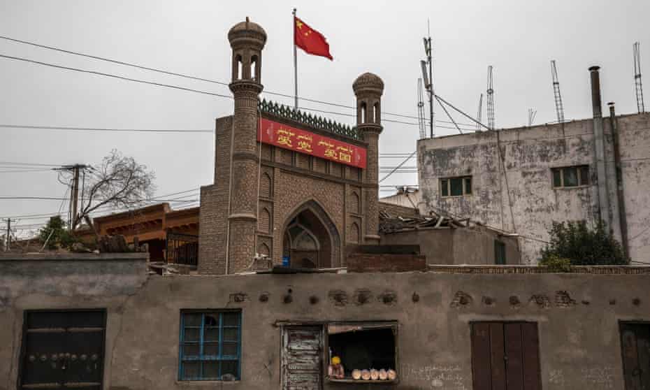 A Chinese flag flies over a local mosque recently closed by authorities as an ethnic Uyghur woman sells bread at her bakery on June 28, 2017 in the old town of Kashgar.