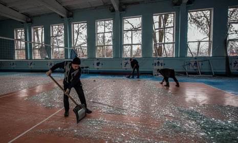 Three people use shovels and brooms to clear away fragments of glass on the floor of a large hall