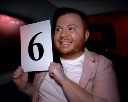 A man holds up a sign with a ‘6’ on it