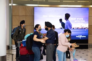 A woman in a dark shirt and mask embraces a man in a dark shirt, mask and dastar, with other family members around them. Rishm Sing meets her family after arriving at Sydney airport from Toronto, Canada.