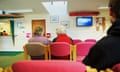 Three patients - two of them older patients - sit in GP surgery waiting room on pink chairs