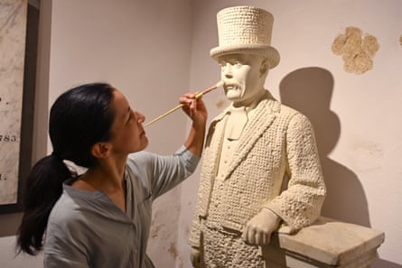 Price applies brush to upper lip of statue of Croft smartly dressed with top hat