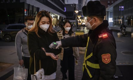 A woman in Beijing has her temperature checked before entering a shopping mall