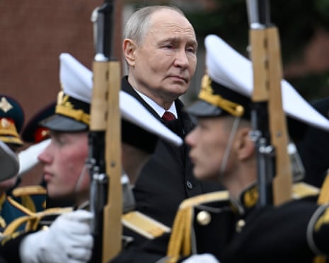 Vladimir Putin stands among military personnel holding rifles with white caps